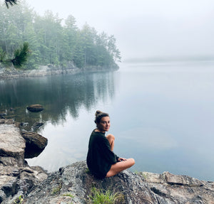 Young woman sitting on a calm foggy lake shore at dawn 