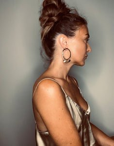 Elegant profile of a woman with a high bun hairstyle, wearing a satin slip dress and statement hoop earrings.