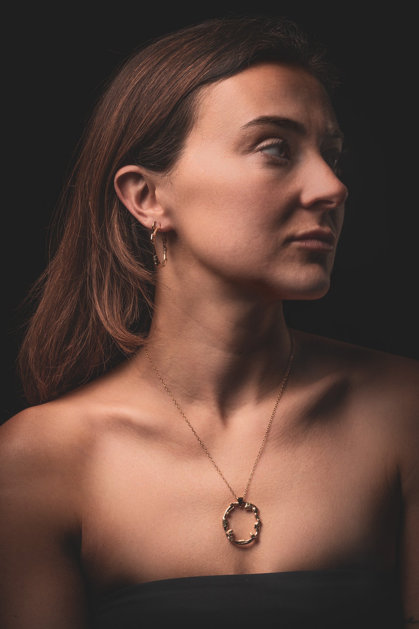Portrait of a woman showcasing the 'Taormina' collection by 'What If You Stayed', featuring handcrafted gold necklace and earrings against a dark background.