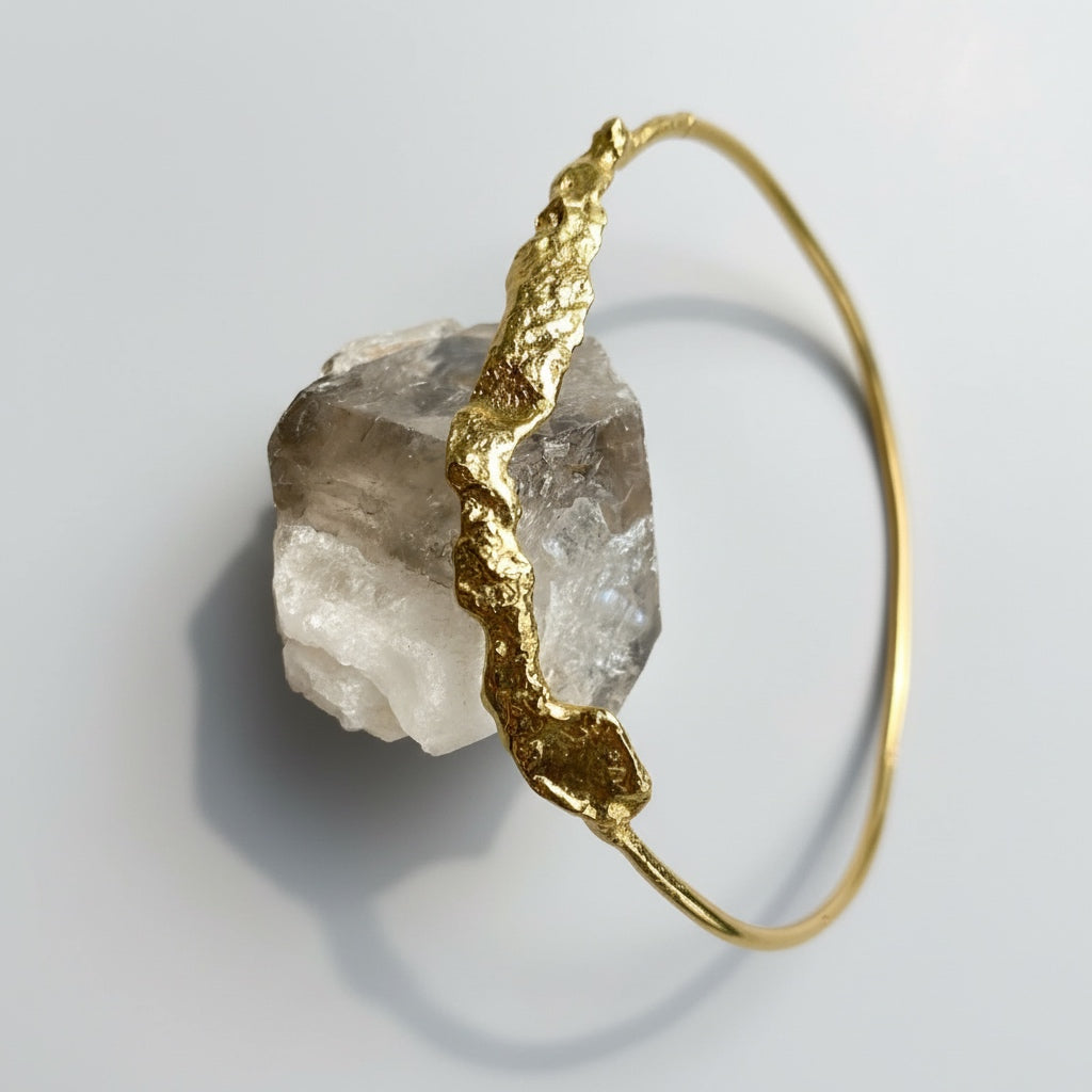 Gold bracelet with a rough crystal stone on a light gray background