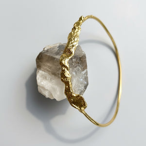 Gold bracelet with a rough crystal stone on a light gray background