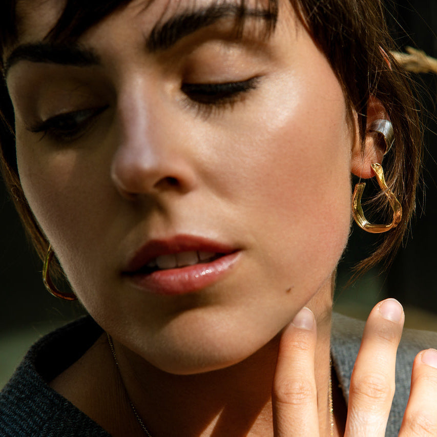 Young Woman with Dark Hair Wearing Gold Ribbon Earrings and Gold Necklace From What If You Stayed Jewelry 