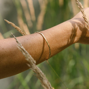 Close-up of a person's arm with a gold bracelet made by what if you stayed against a blurred natural background