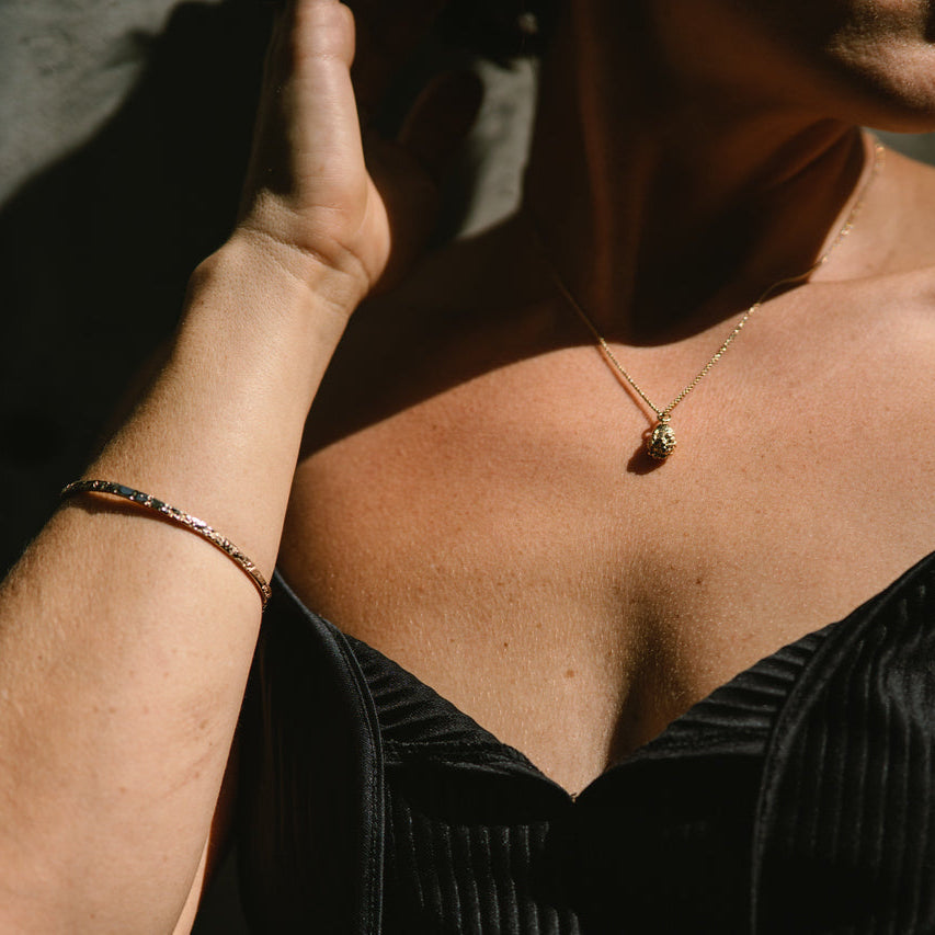 Person wearing a necklace with a drop shape pendant, and a gold bangle made by what if you stayed