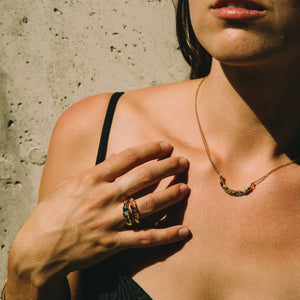 Woman wearing a gold necklace with raw stones and gold rings with raw sapphires made by What If You Stayed against a concrete wall