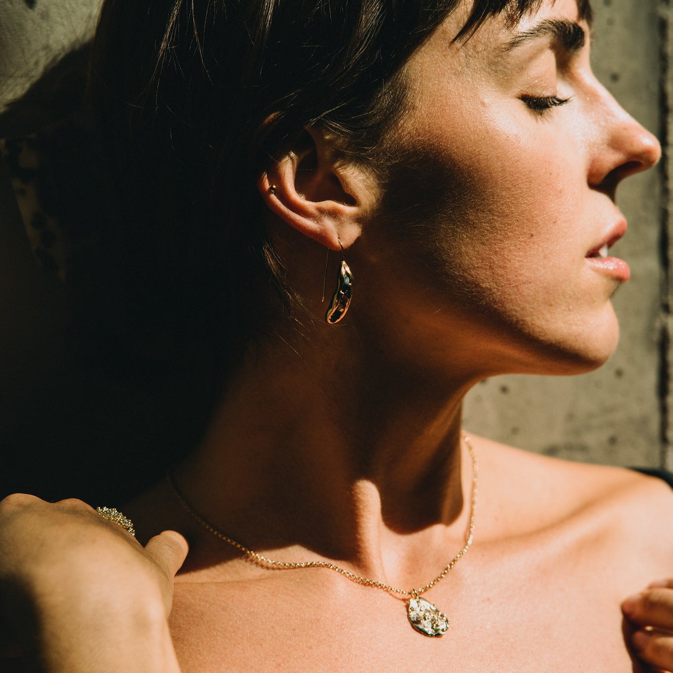 Woman with short hair wearing a gold necklace against a textured wall.