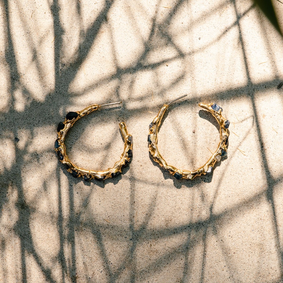 Gold hoop earrings with raw blue sapphires made by what if you stayed on a light textured background