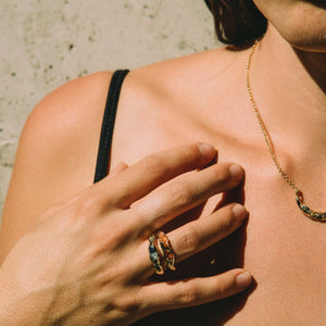Person wearing a black top and gold necklace with rings, against a neutral background