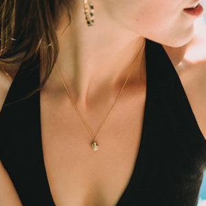 Close-up of a gold necklace with a pendant  made by what if you stayed on a person wearing a black top.