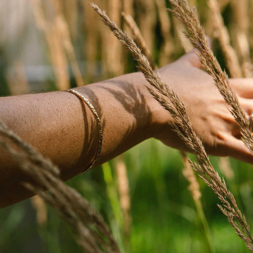 Hand with gold bracelet made by what if you stayed touching tall grass