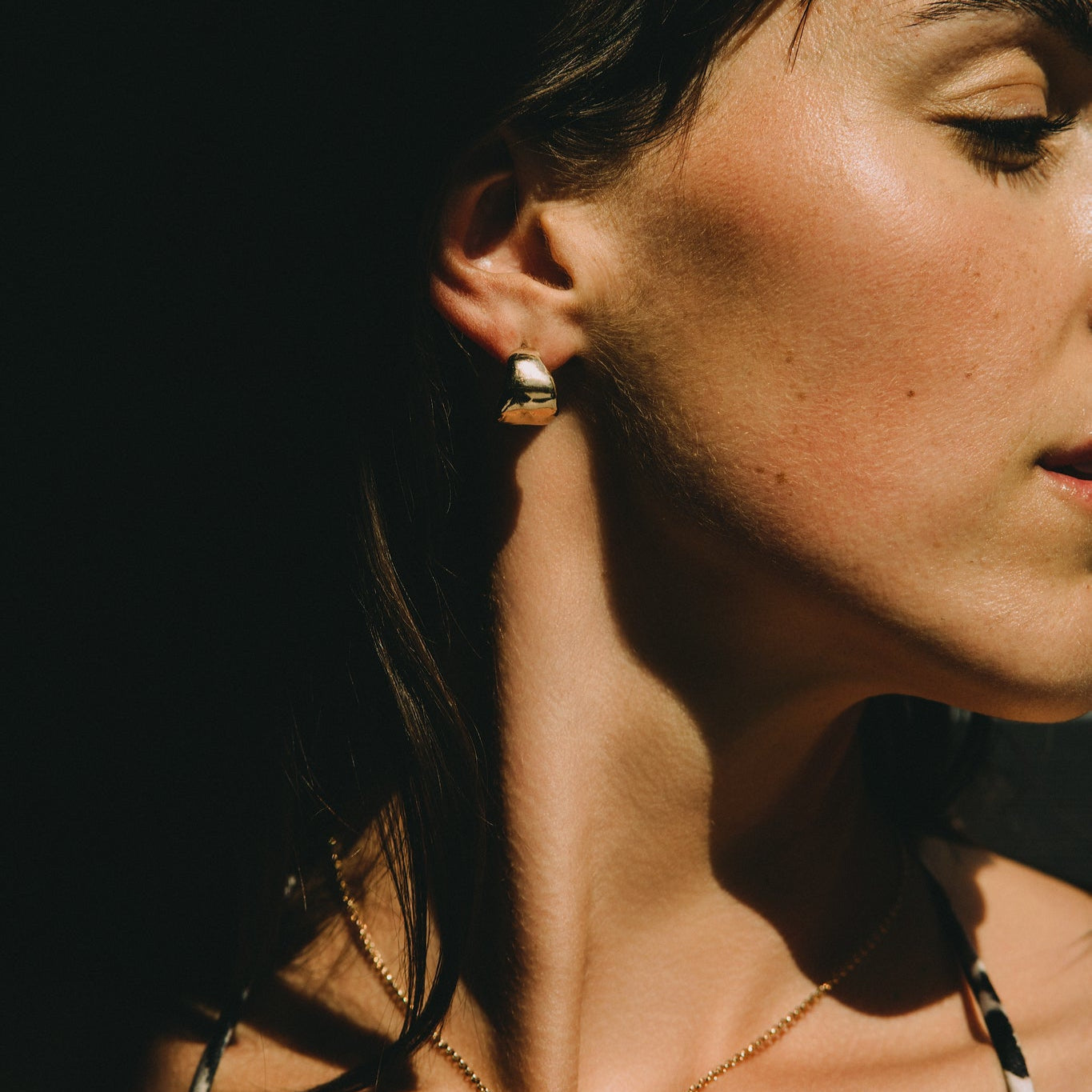 Woman wearing a leopard print top against a dark background with a gold necklace textured and small earrings hoops minimalist style made by what if you stayed jewelry