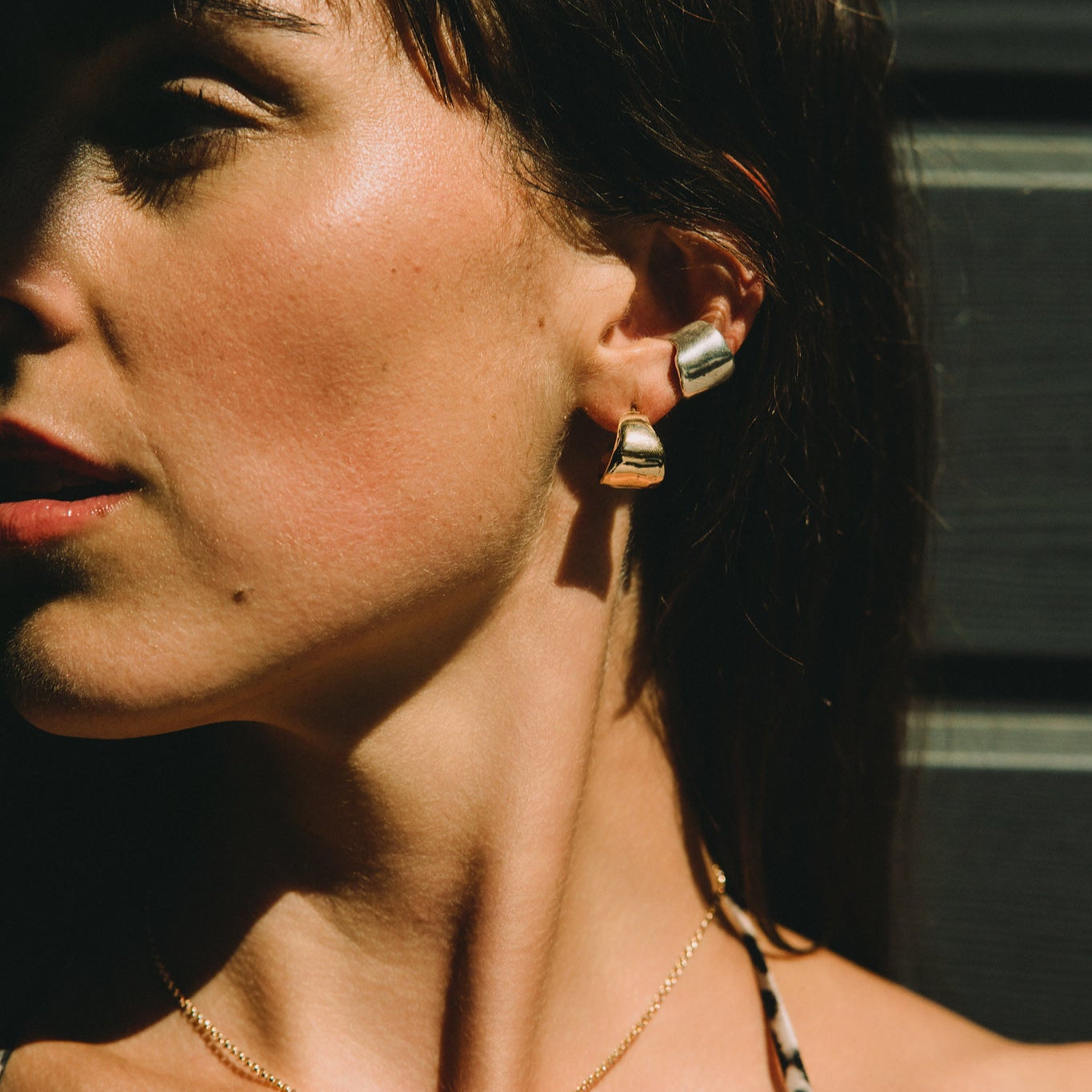 Woman wearing a leopard print top against a dark background with a gold necklace textured and small earrings hoops minimalist style made by what if you stayed jewelry