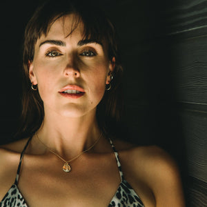 Woman wearing a leopard print top against a dark background with a gold necklace textured and small earrings hoops minimalist style made by what if you stayed jewelry