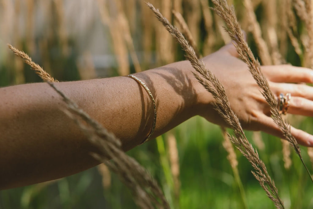 Video of a woman's and in wheat grass wearing a gold bangle made by what if you stayed