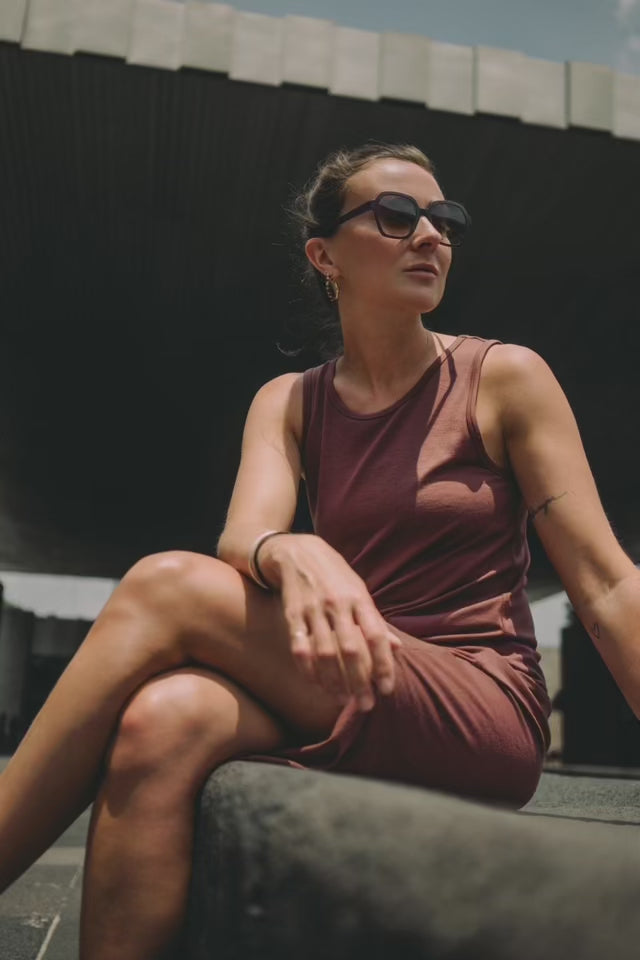 Young woman sitting in the sun at an architectural place wearing a sun dress and gold jewelry made by what if you stayed 