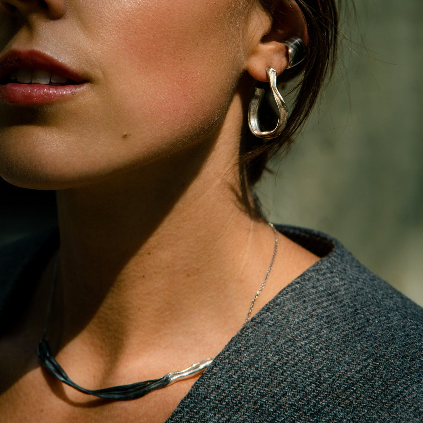 Close-up of a woman wearing silver hoop earrings and necklace made by what if you stayed with a blurred background