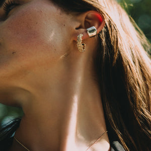 Close-up of a person wearing gold earrings with a blurred natural background