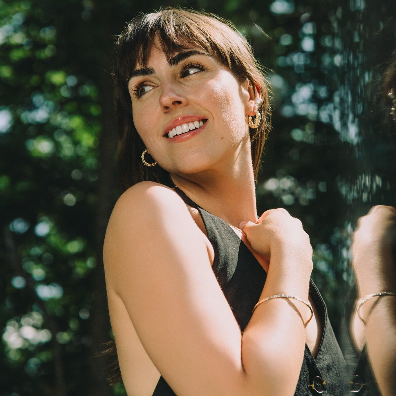 Woman smiling outdoors with greenery in the background