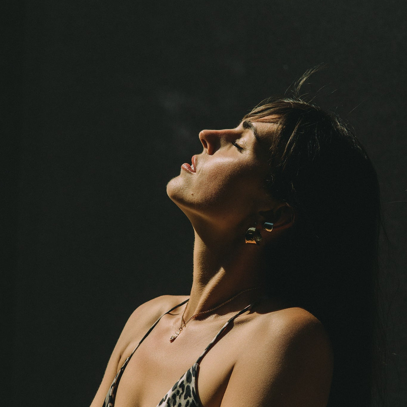 Woman with closed eyes against a dark background wearing large earrings hoops in gold and silver earcuff made by what if you stayed