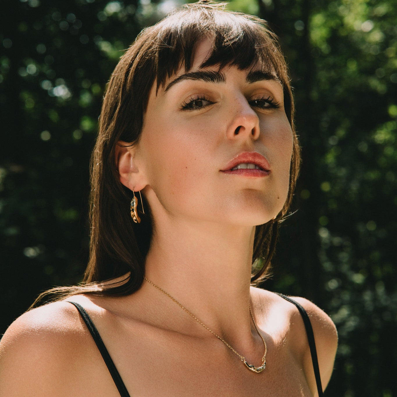 Young woman in sunlight outdoor wearing a black top with gold jewellery made by What If You Stayed