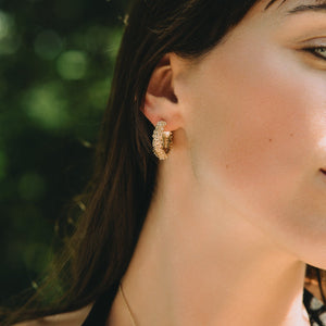 Close-up of a woman wearing a gold earring with a blurred green background