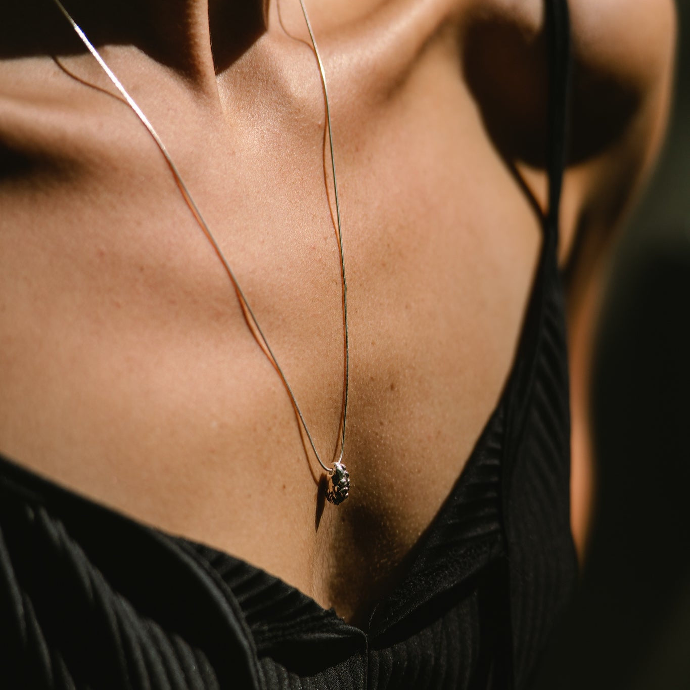 Close-up of a silver necklace made by what if you stayed with a pendant on a person wearing a black top.