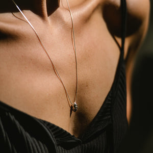 Close-up of a silver necklace made by what if you stayed with a pendant on a person wearing a black top.