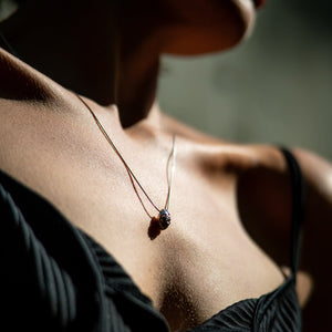 Close-up of a necklace with a  silver pendant  made by what if you stayed on a person wearing a black top.